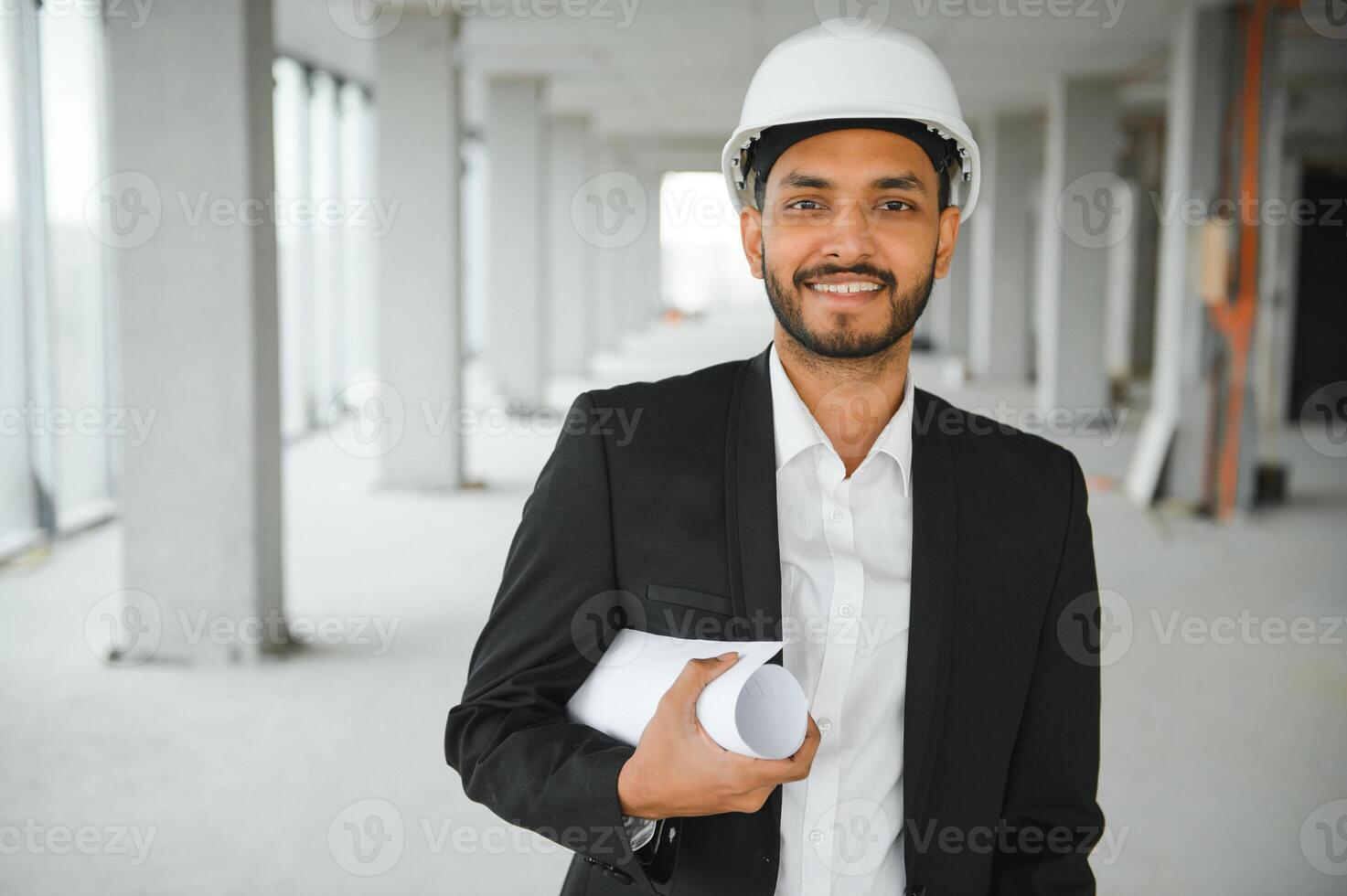 Indian construction site manager standing wearing helmet, thinking at construction site. Portrait of mixed race manual worker or architect. photo