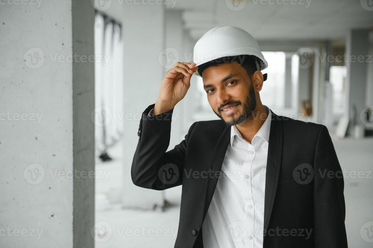 Indian construction site manager standing wearing helmet, thinking at construction site. Portrait of mixed race manual worker or architect. photo