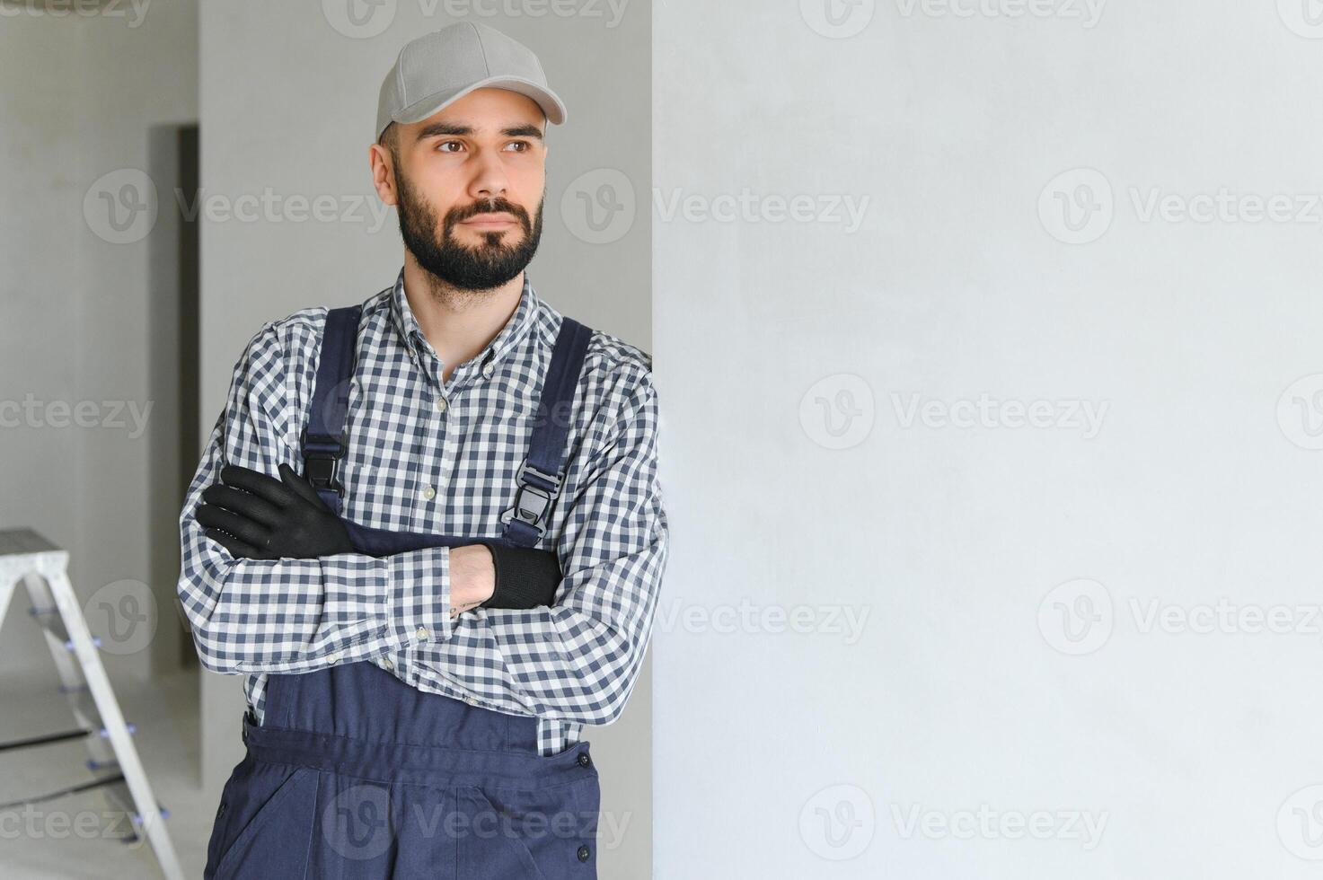 Portrait of handsome mechanic with stubble in blue overall, shirt having his arms crossed, looking at camera photo