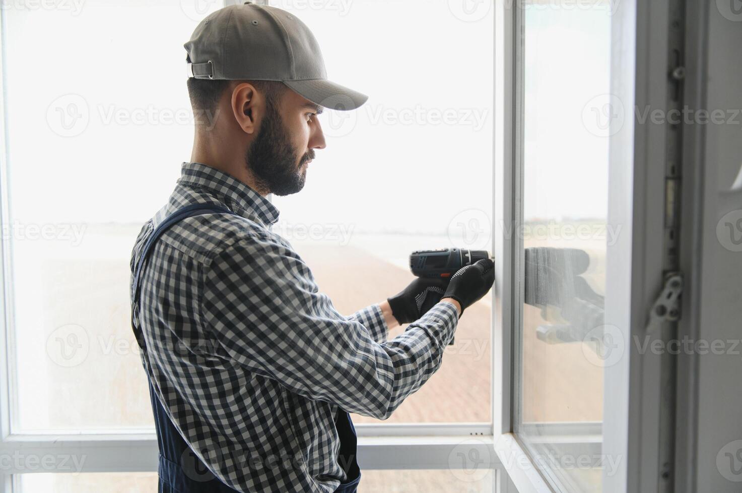 Workman in overalls installing or adjusting plastic windows in the living room at home photo