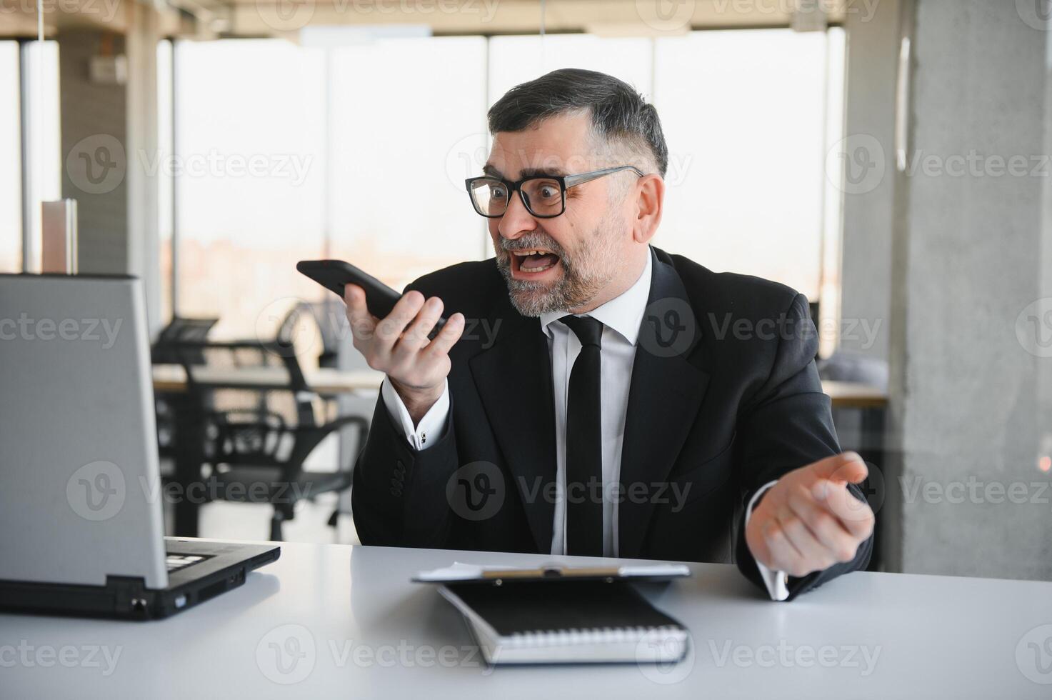 stressed handsome businessman working at desk in modern office shouting at laptop screen and being angry about financial situation, jealous of rival capabilities, unable to meet client needs photo