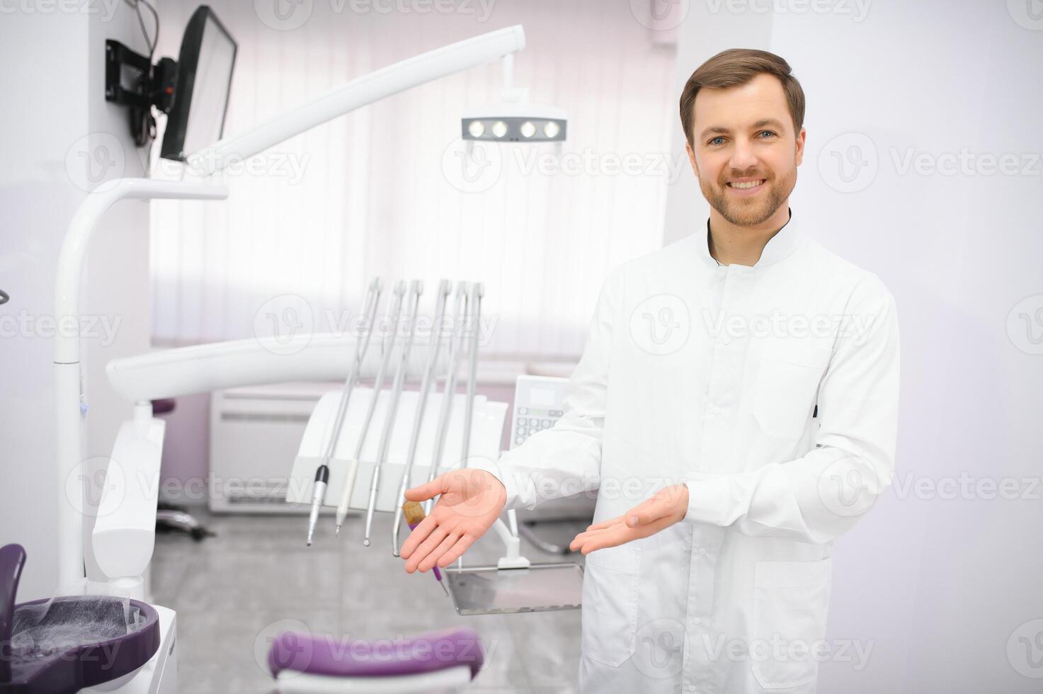 Attractive male dentist in doctors white lab coat posing in modern dental office photo