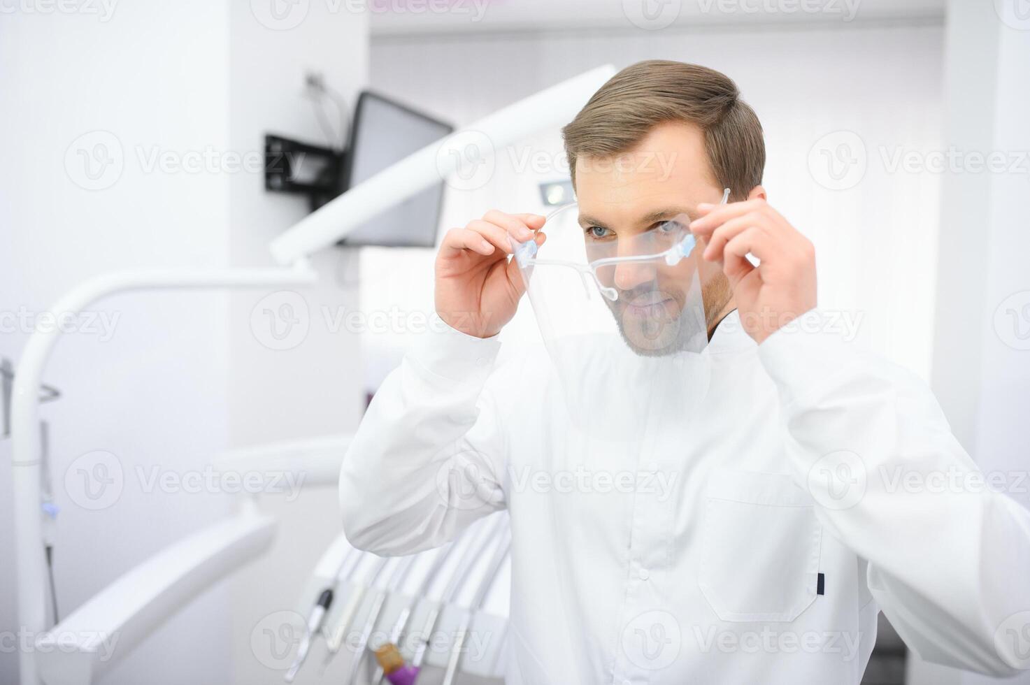Attractive male dentist in doctors white lab coat posing in modern dental office photo