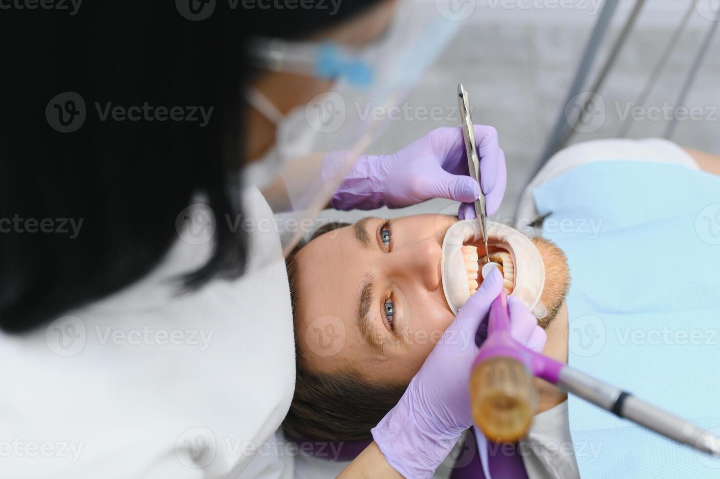 Periodontal Services. Closeup Shot Of Smiling Man Getting Treatment In Stomatologic Clinic, Dentist Doctor In Gloves Using Sterile Dental Tools For Examining Teeth Of Male Patient photo