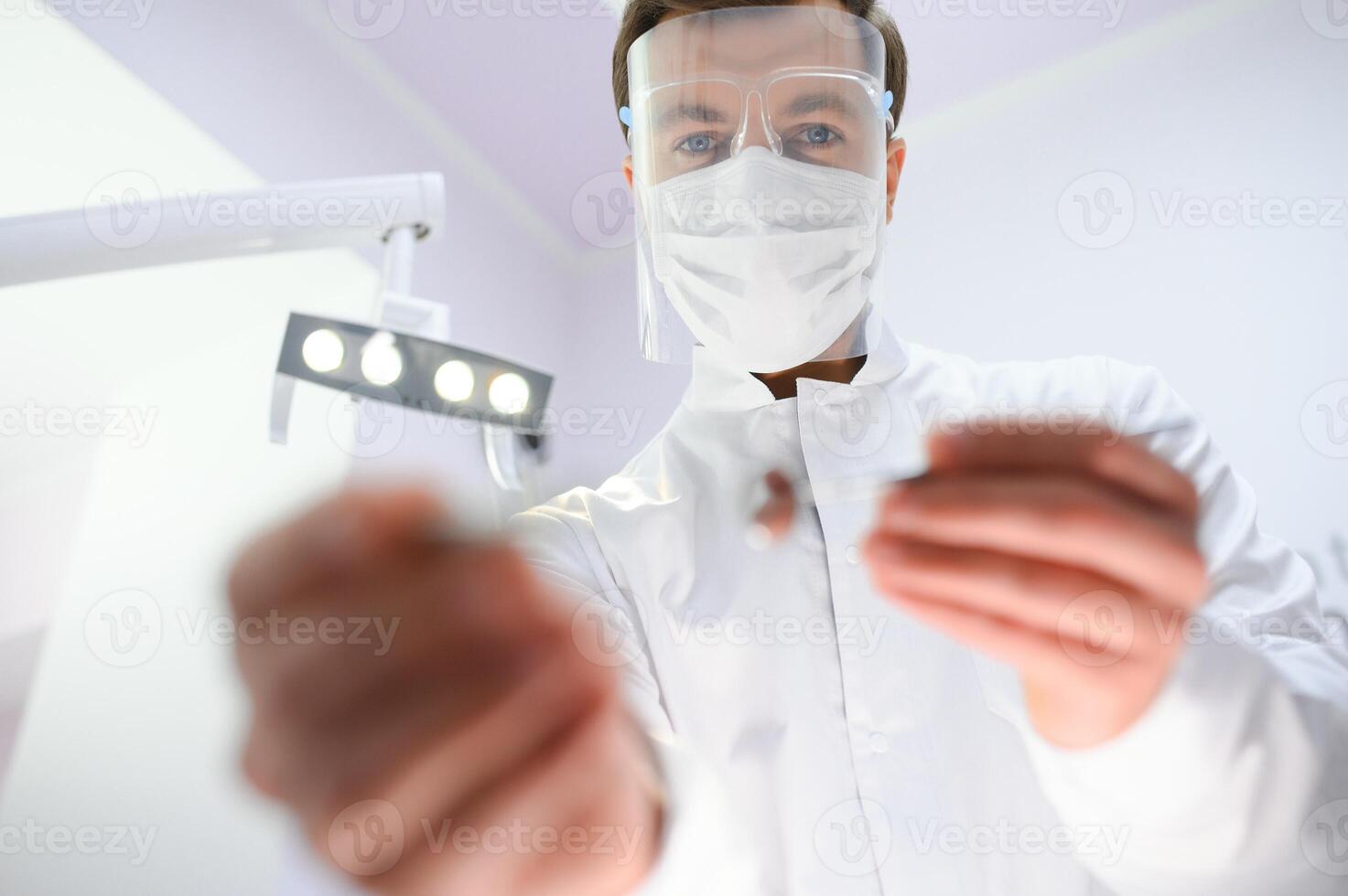 Bottom view young confident happy professional stomatologist european doctor man 20s in white gown hold showing tooth drilling machine at dentist office indoor cabinet. Healthcare aesthetic treatment. photo