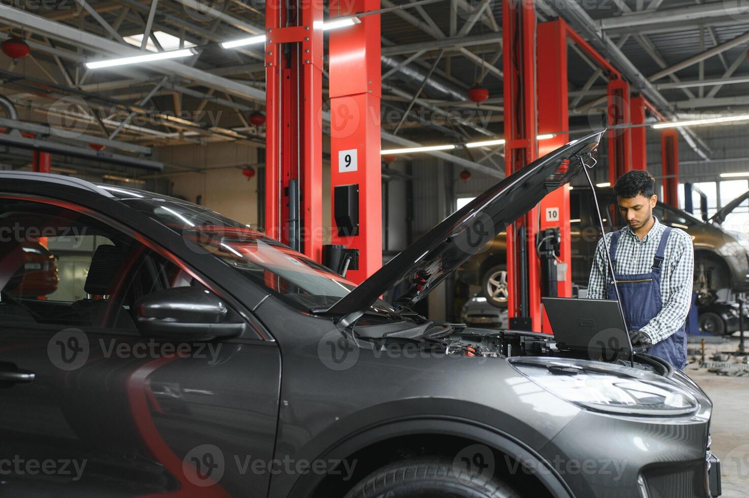 Mechanic man mechanic manager worker using a laptop computer checking car in workshop at auto car repair service center. Engineer young man looking at inspection vehicle details under car hood. photo