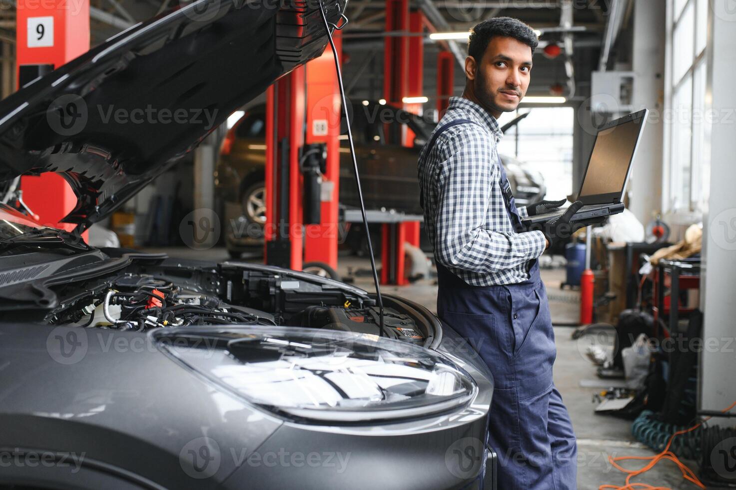 Mechanic man mechanic manager worker using a laptop computer checking car in workshop at auto car repair service center. Engineer young man looking at inspection vehicle details under car hood. photo