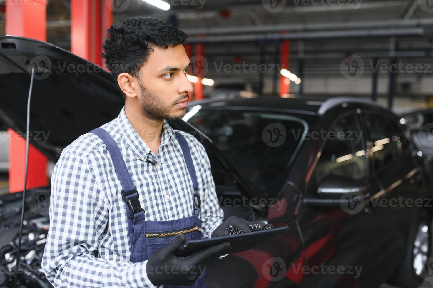 Mechanic man mechanic manager worker using a laptop computer checking car in workshop at auto car repair service center. Engineer young man looking at inspection vehicle details under car hood. photo