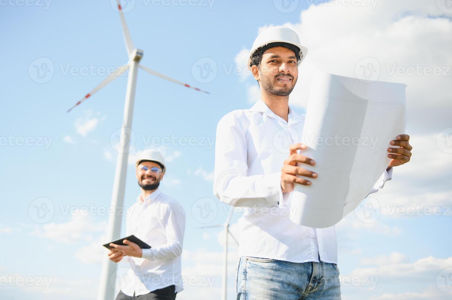 Two engineers discussing against turbines on wind turbine farm. photo