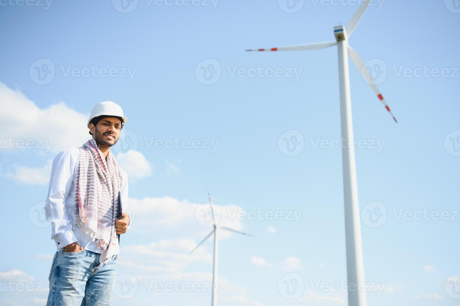 Engineer India man working at windmill farm Generating electricity clean energy. Wind turbine farm generator by alternative green energy. Asian engineer checking control electric power photo
