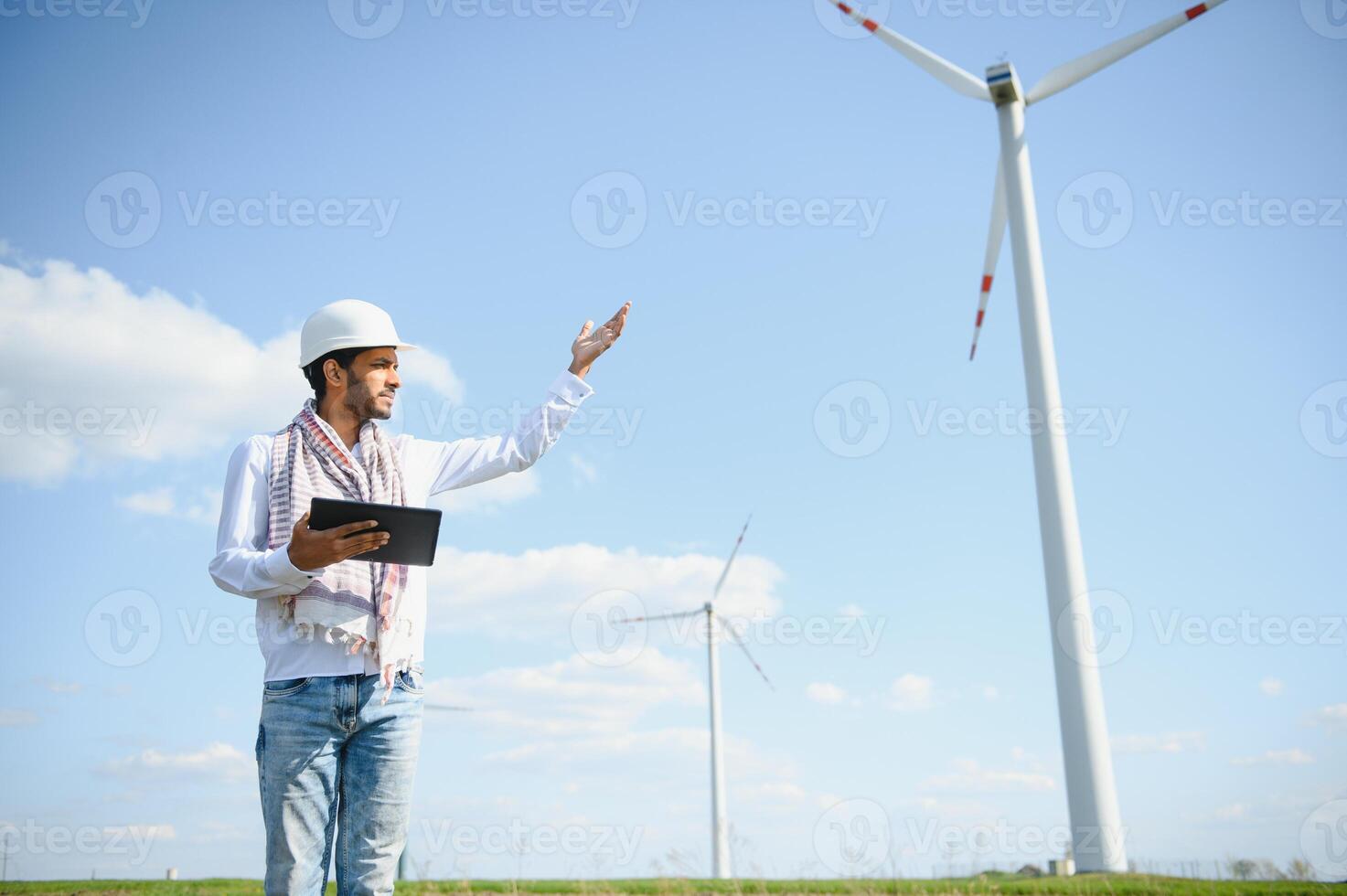 Engineer India man working at windmill farm Generating electricity clean energy. Wind turbine farm generator by alternative green energy. Asian engineer checking control electric power photo