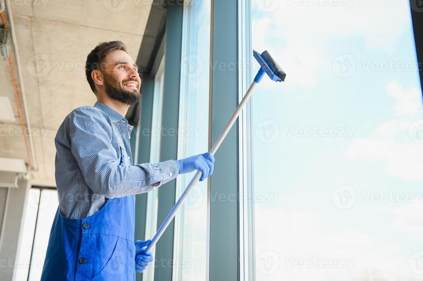 Male professional cleaning service worker in overalls cleans the windows and shop windows of a store with special equipment photo