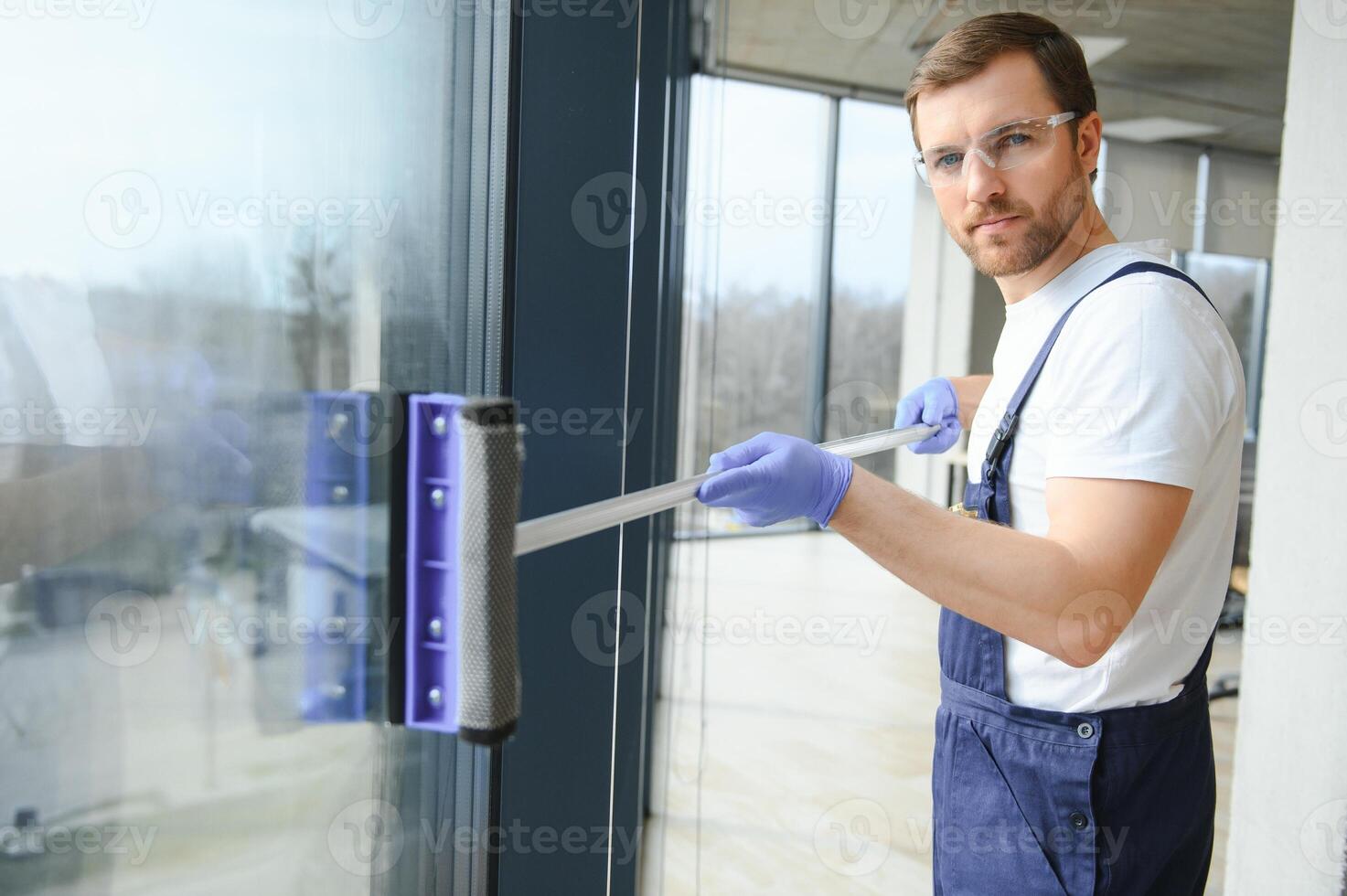 Male professional cleaning service worker in overalls cleans the windows and shop windows of a store with special equipment. photo