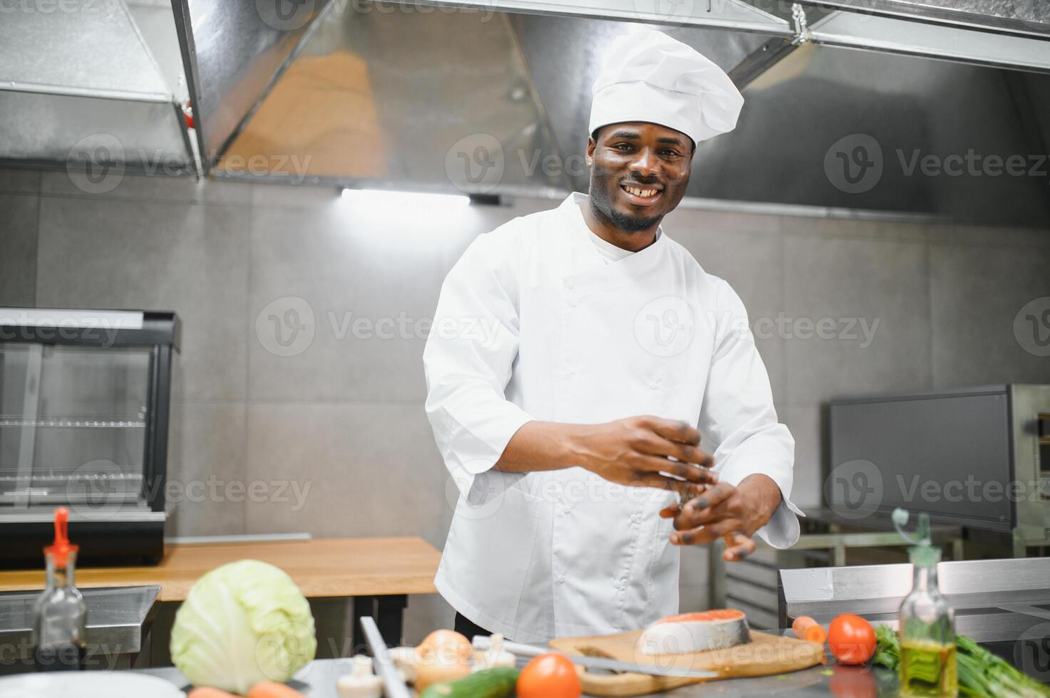 Experienced professional African-American chef standing in kitchen of restaurant with working staff photo