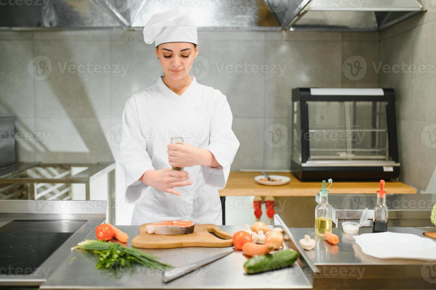 young beautiful female chef cooks salmon in restaurant kitchen photo