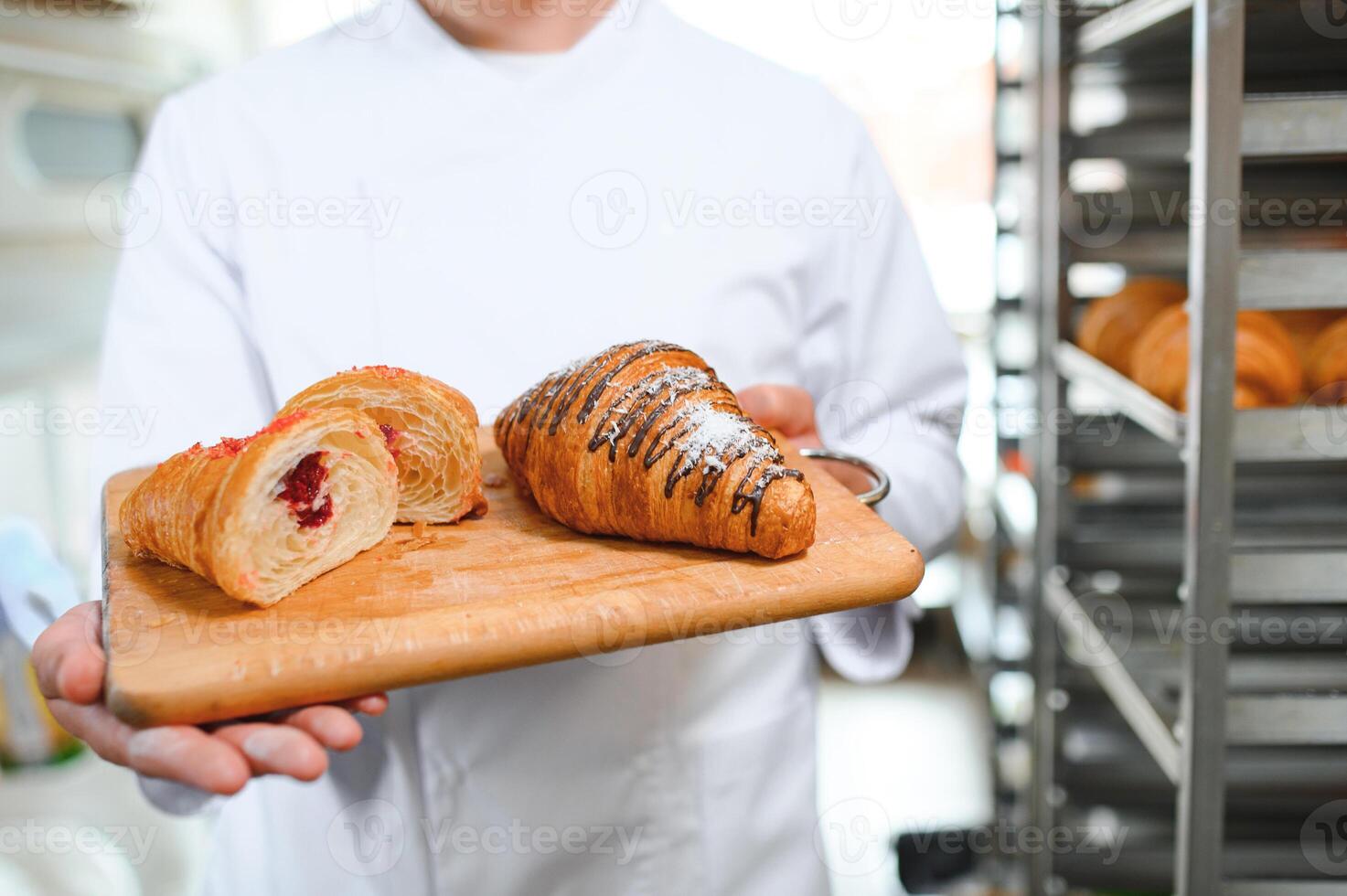 A baker cuts a croissant in a bakery and shows the jam filling photo