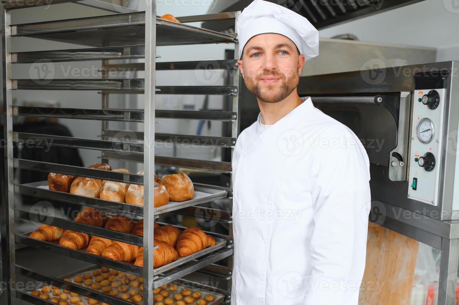 Happy baker standing near tray with bread at the bakery photo
