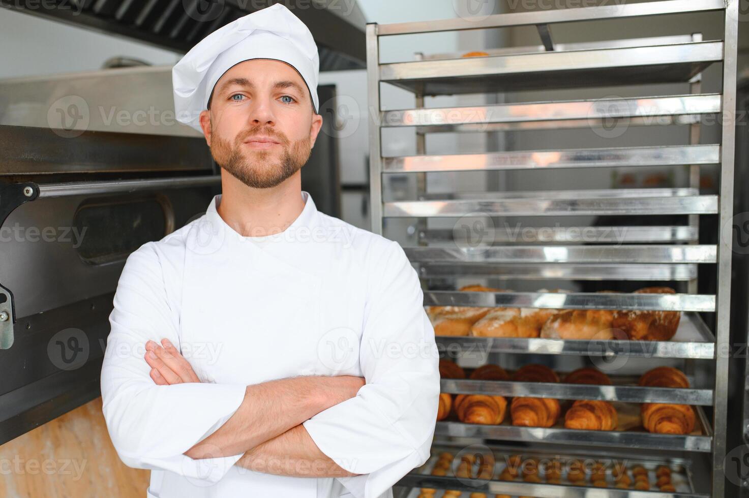 Happy baker standing near tray with bread at the bakery photo