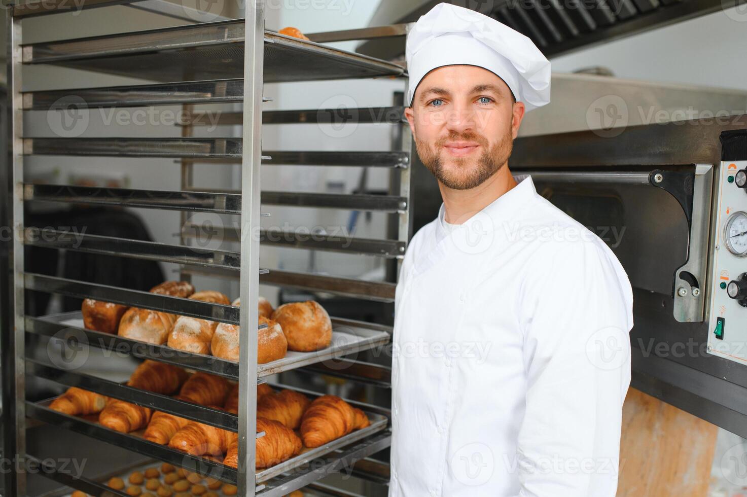 Happy baker standing near tray with bread at the bakery photo