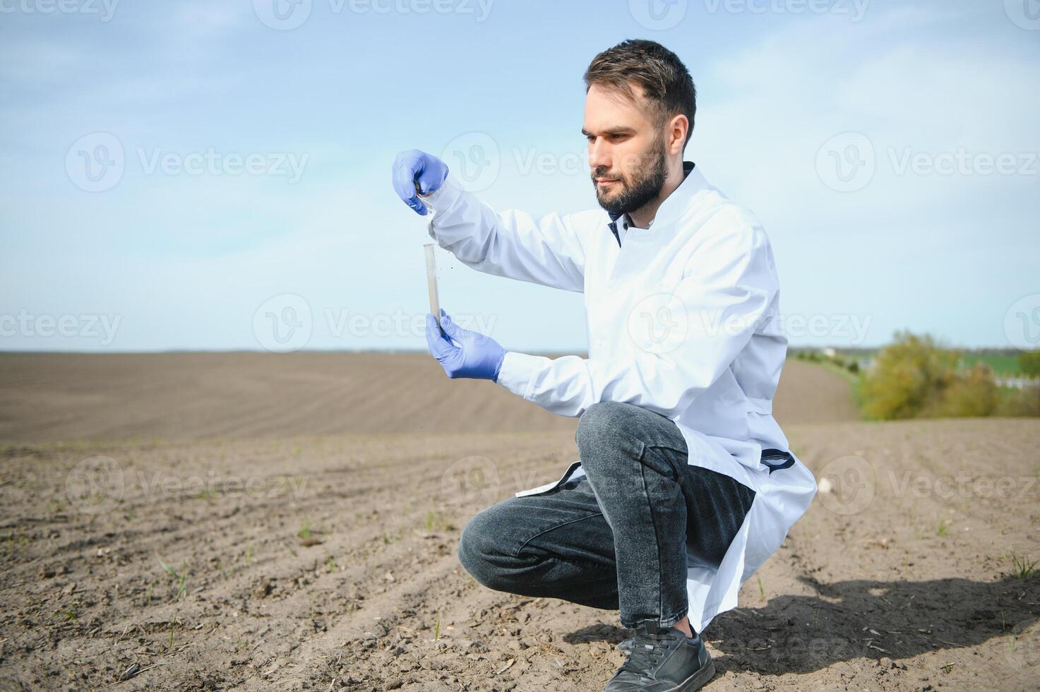 Laboratory worker holding professional glassware and testing black soil after harvest in the field photo