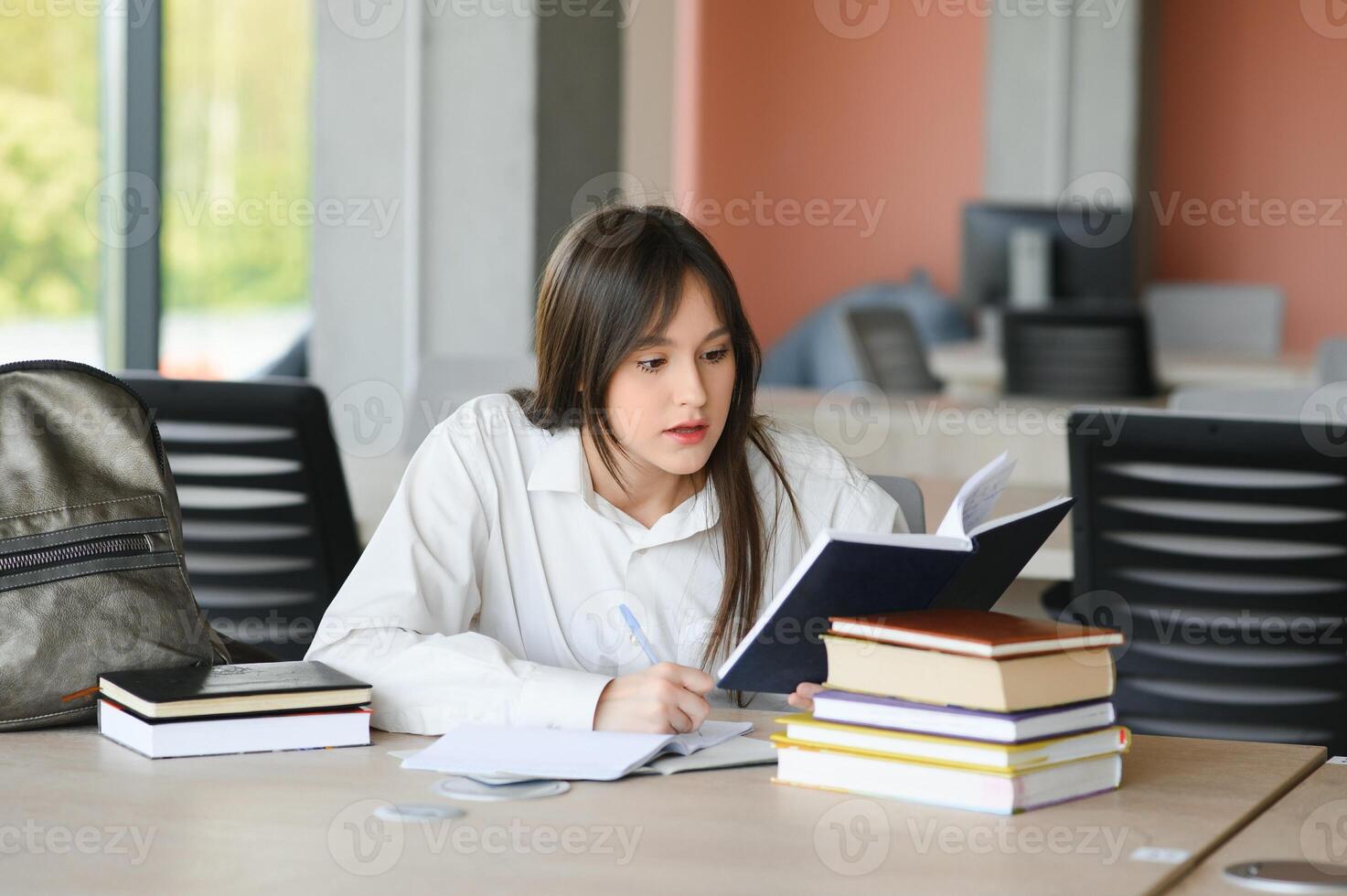 Teen girl studying with textbook writing essay learning in classroom. photo