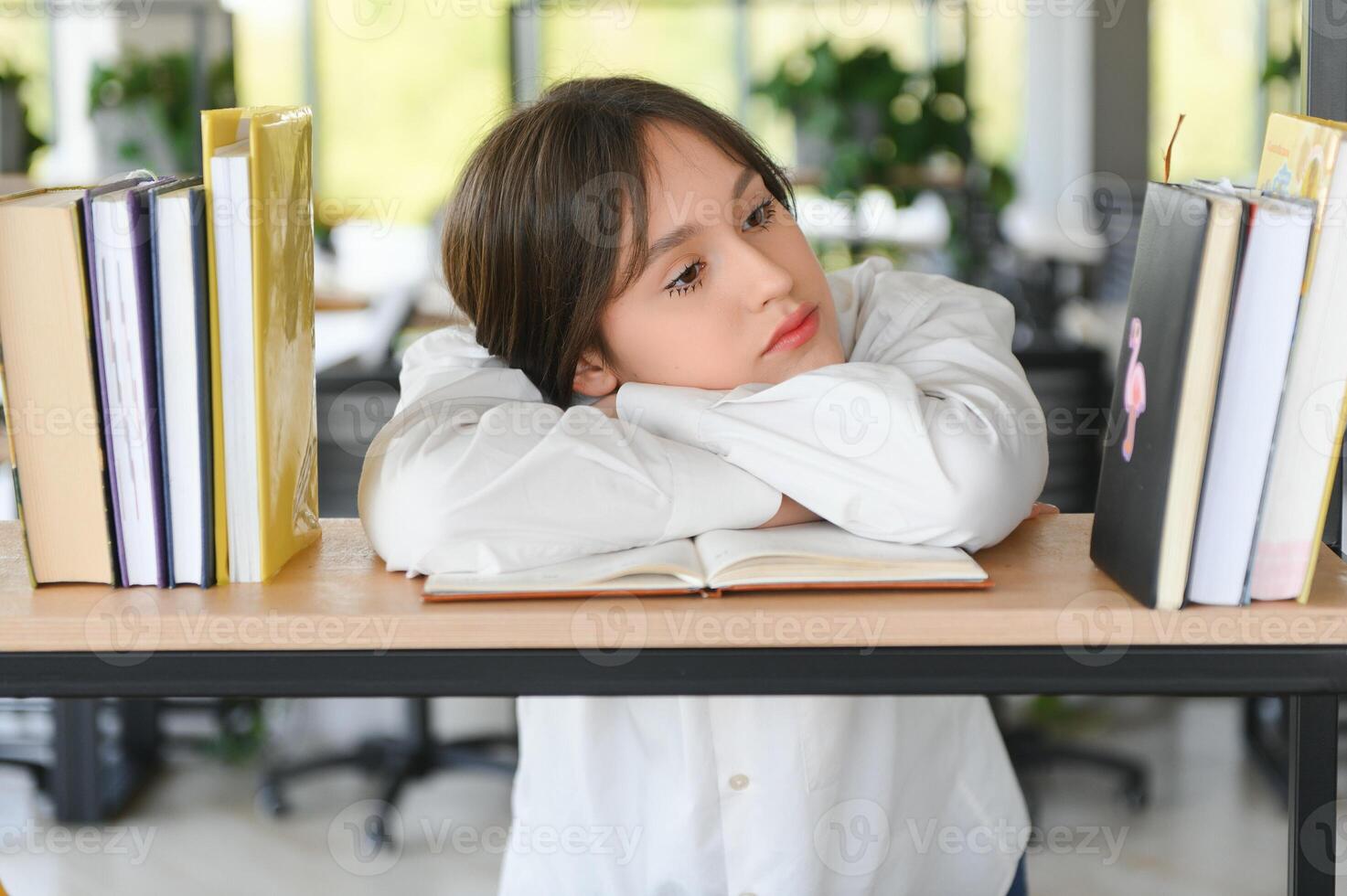 A cute 15-year-old schoolgirl sits at a school desk with notebooks and books and studies photo