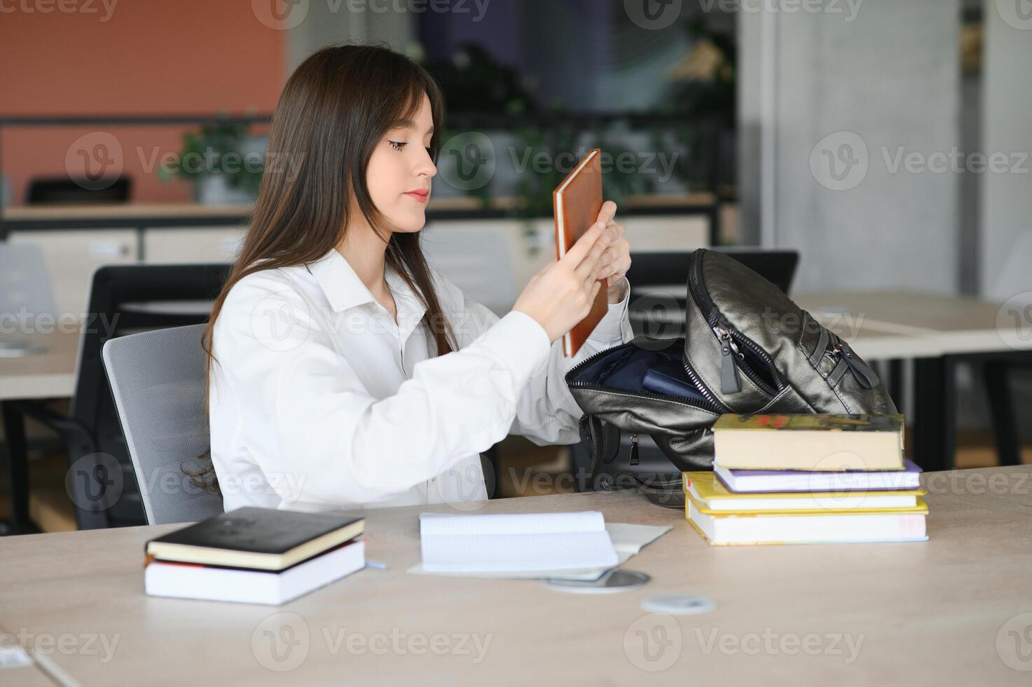 Teen girl studying with textbook writing essay learning in classroom. photo