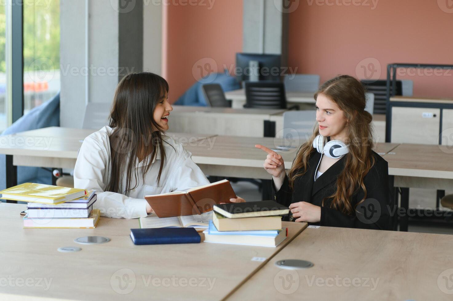 Two fifteen-year-old schoolgirls reading books and taking abstract in copybooks are doing homework in the school library photo