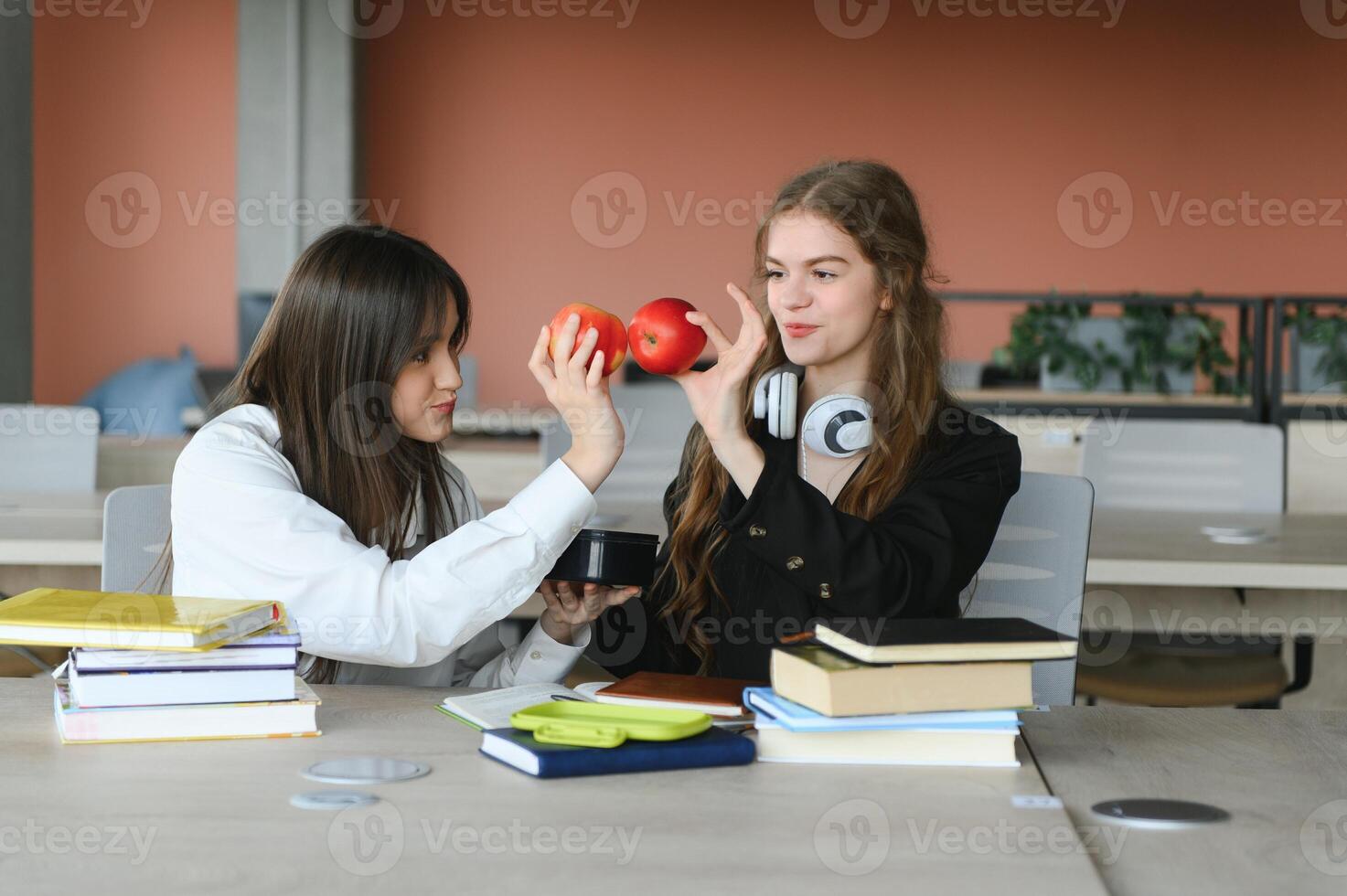 Two fifteen-year-old schoolgirls reading books and taking abstract in copybooks are doing homework in the school library photo