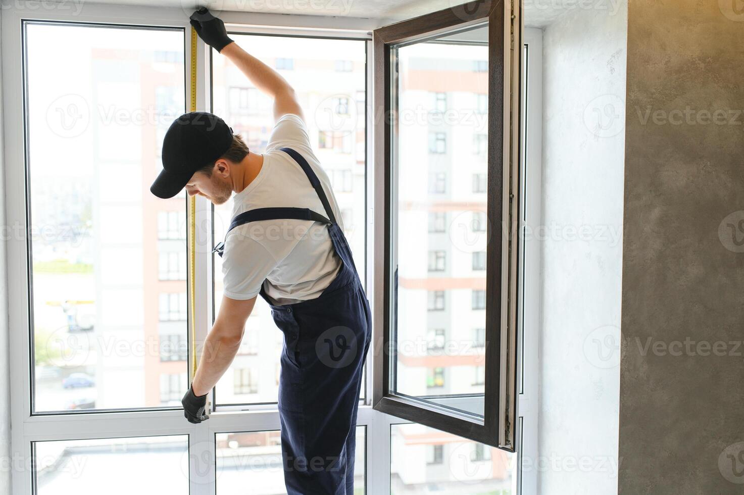 Workman in overalls installing or adjusting plastic windows in the living room at home photo