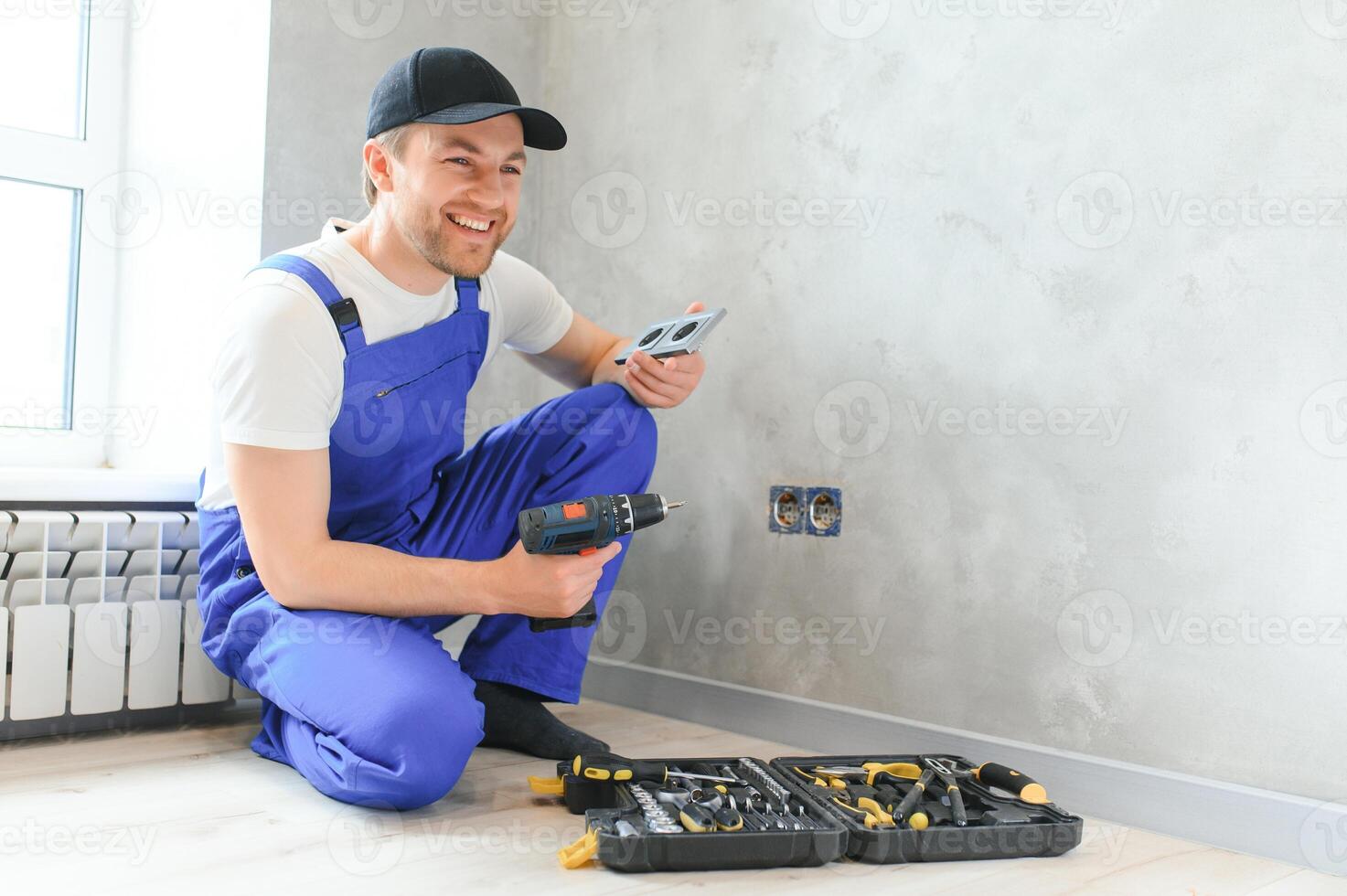 Confident professional electrician in uniform using screwdriver while replacing a socket in apartment after renovation work photo