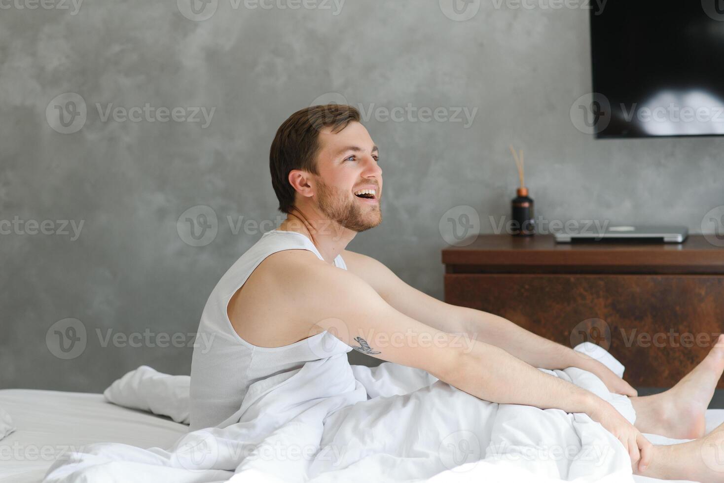 Handsome man laughing lying on his bed at home photo