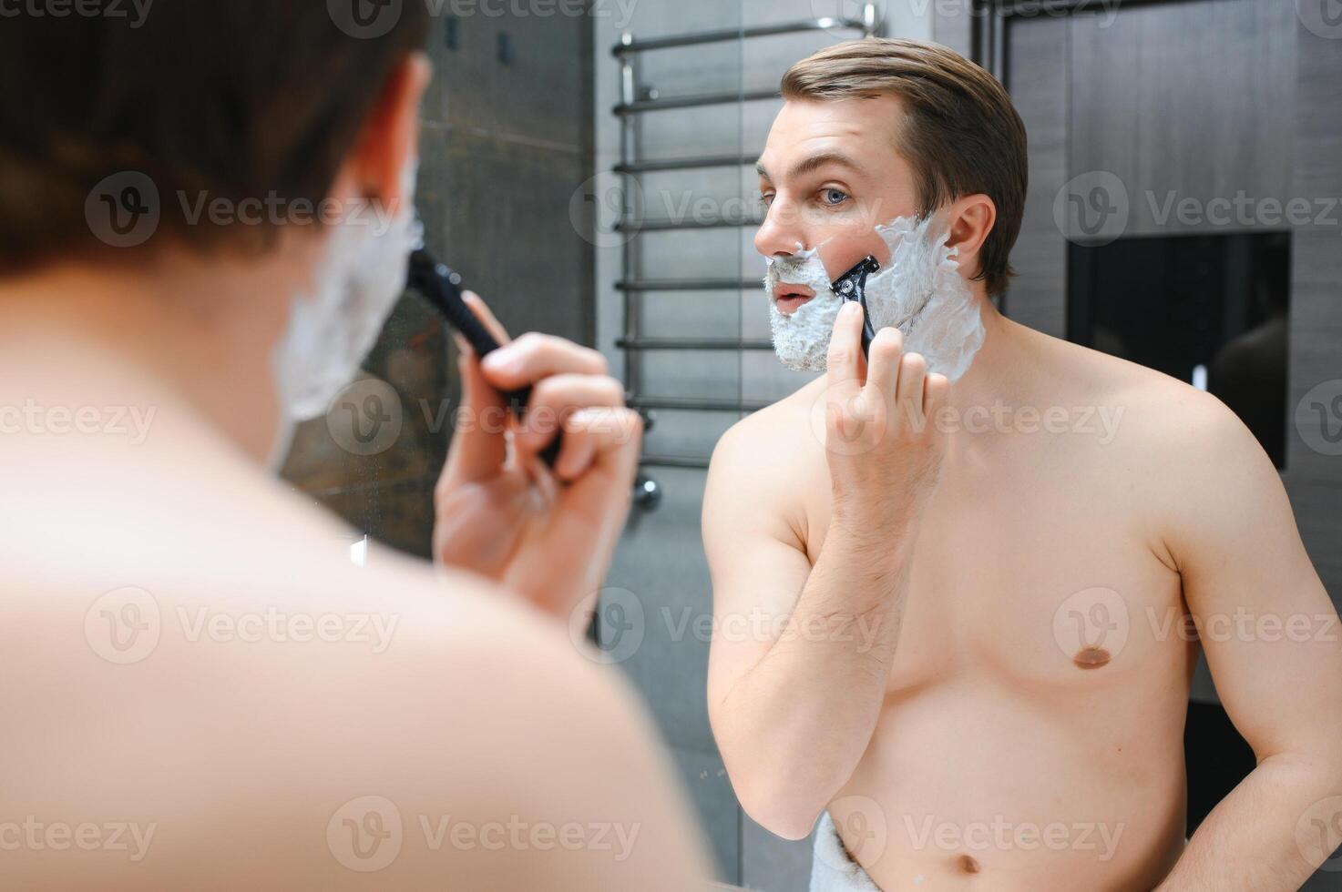 Mature handsome man shaving in front of mirror photo