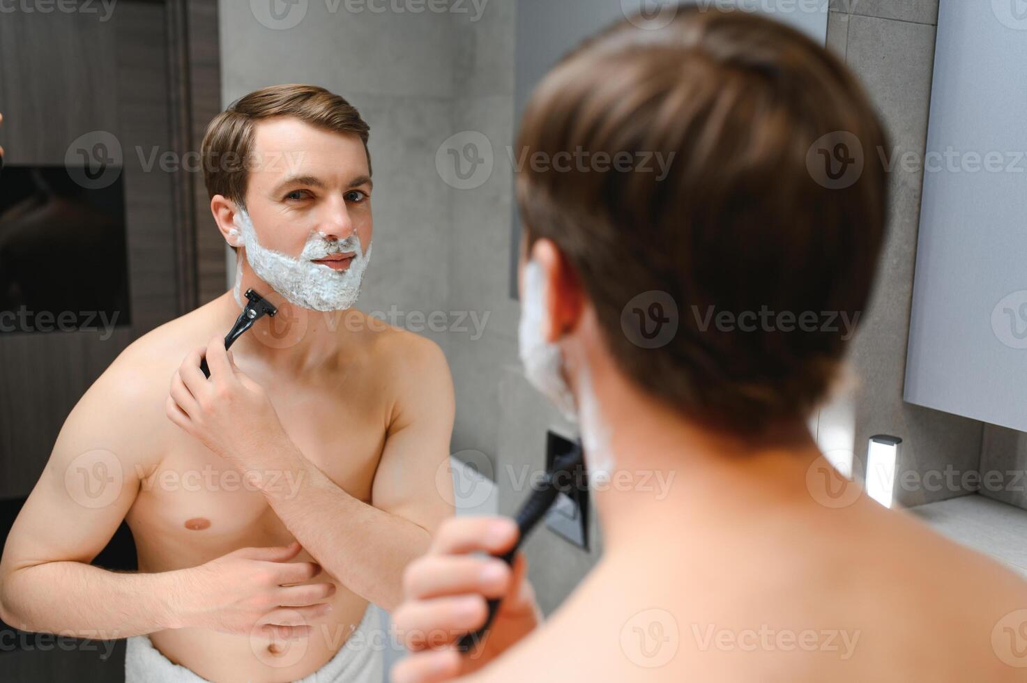 Mature handsome man shaving in front of mirror photo