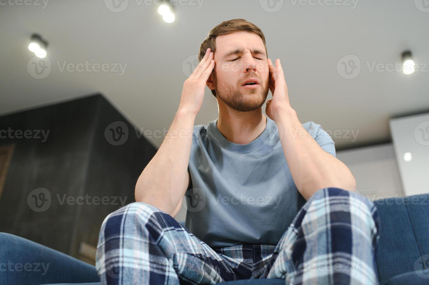 Unpleasant pain. Sad unhappy handsome man sitting on the sofa and holding his forehead while having headache. photo