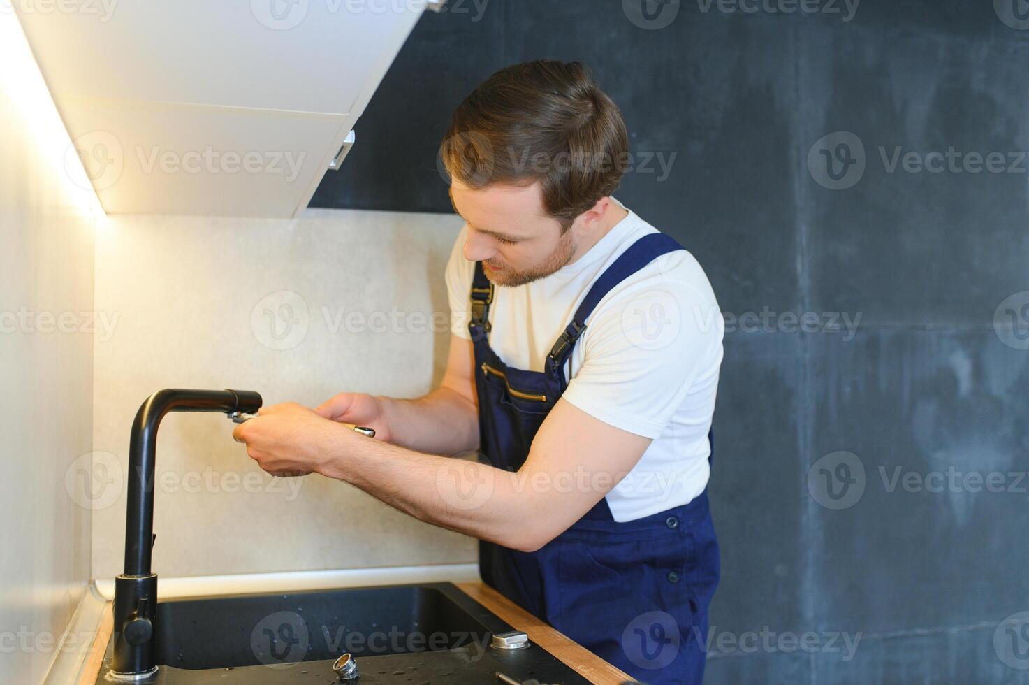 Young Repairman Installing Faucet Of Kitchen Sink In Kitchen Room photo