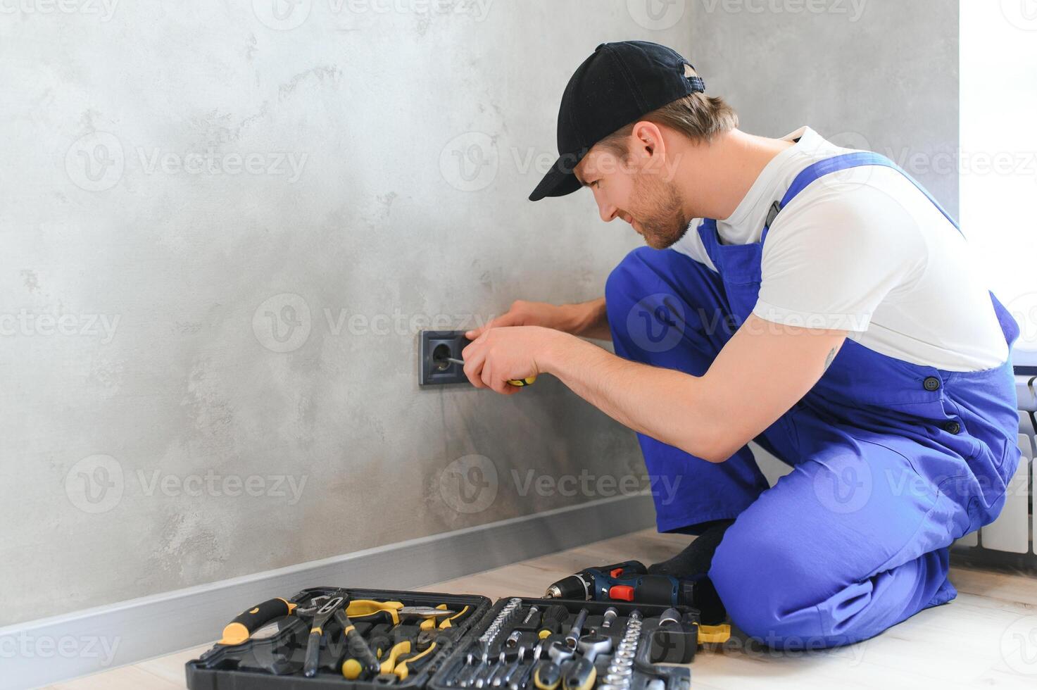 Smiling professional electrician in uniform replacing a socket in apartment after renovation work photo