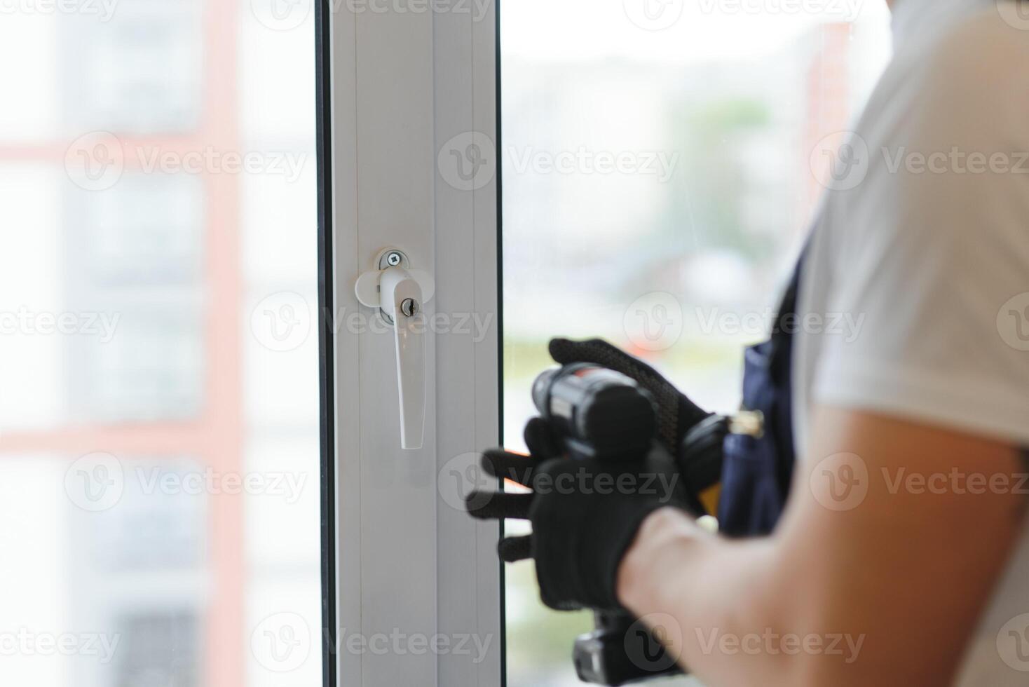 Workman in overalls installing or adjusting plastic windows in the living room at home photo