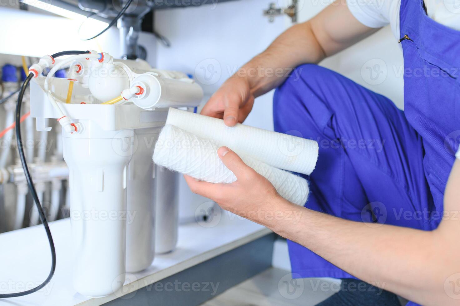 Plumber installs or change water filter. Replacement aqua filter. Repairman installing water filter cartridges in a kitchen. Installation of reverse osmosis water purification system. photo