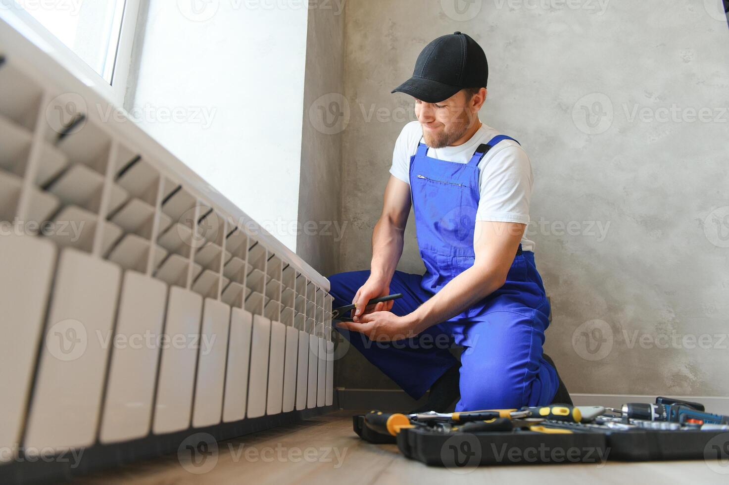 young man plumber checking radiator while installing heating system in apartment photo