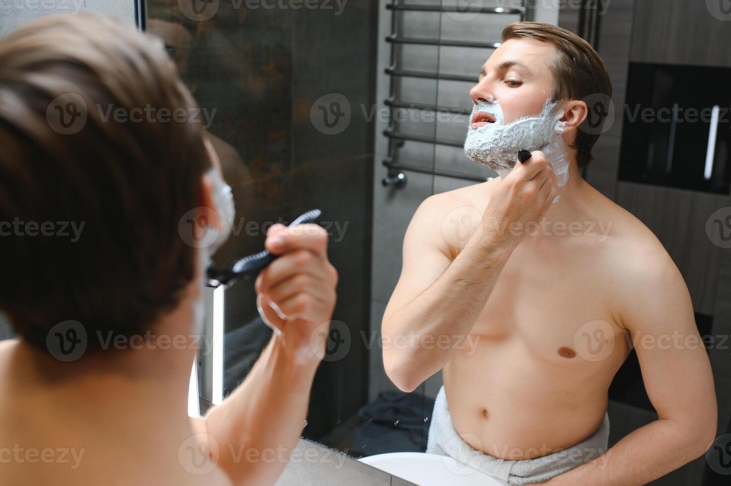 Mature handsome man shaving in front of mirror photo