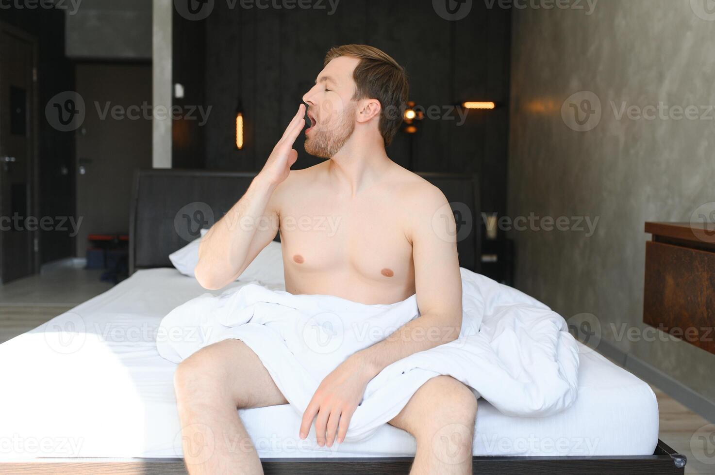 Young man waking up and rise hands stretching on white bed in the morning with sunlight through window photo