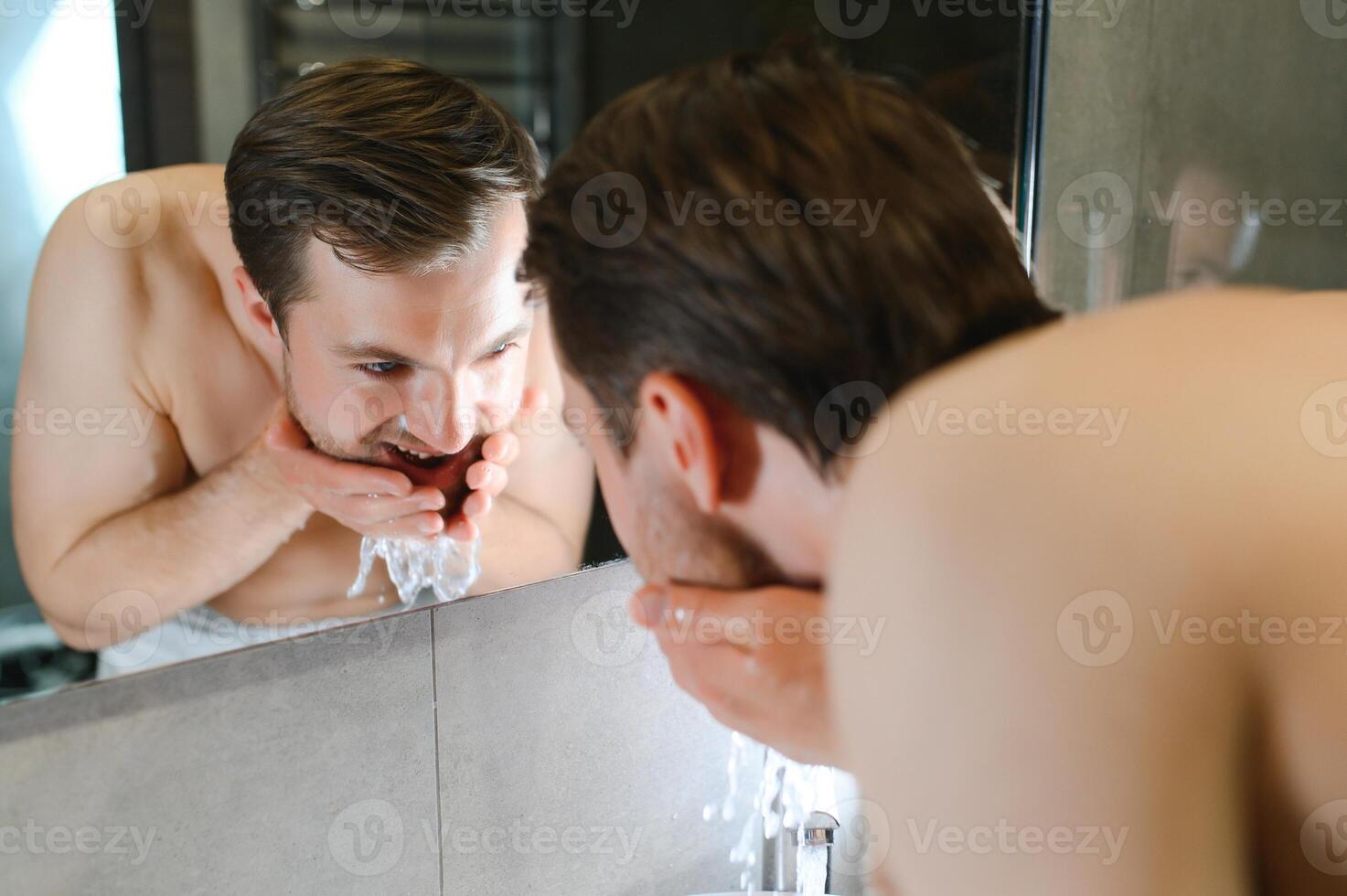 Bright caucasian man spraying water on his face after shaving in the bathroom at home photo
