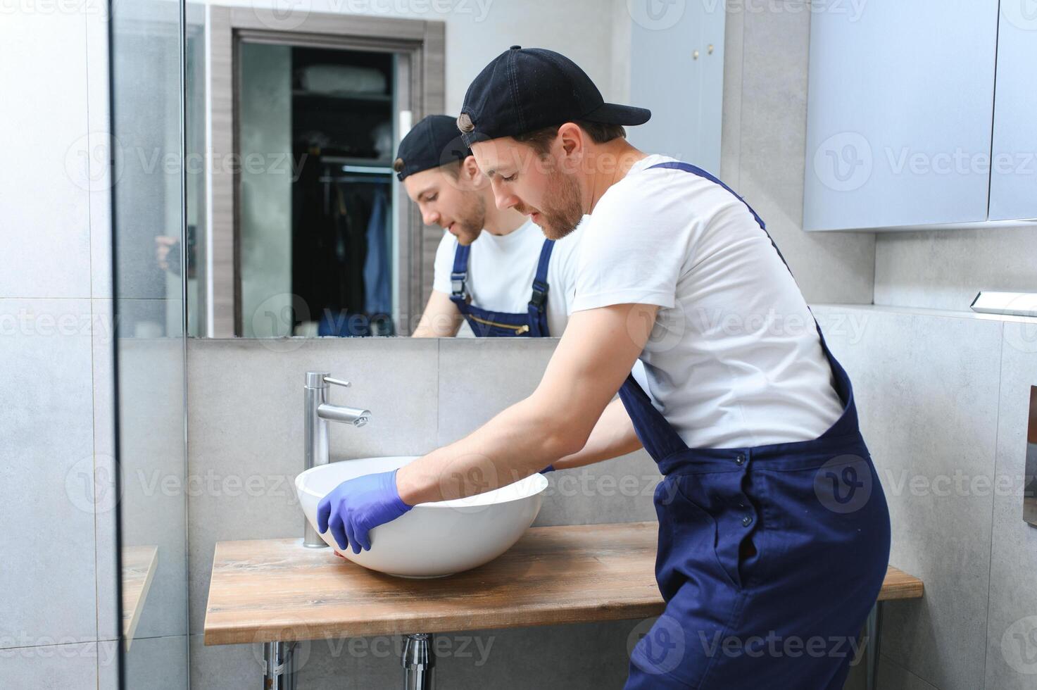 Professional plumber, male worker in uniform installing sink and water pipe in new apartment. photo