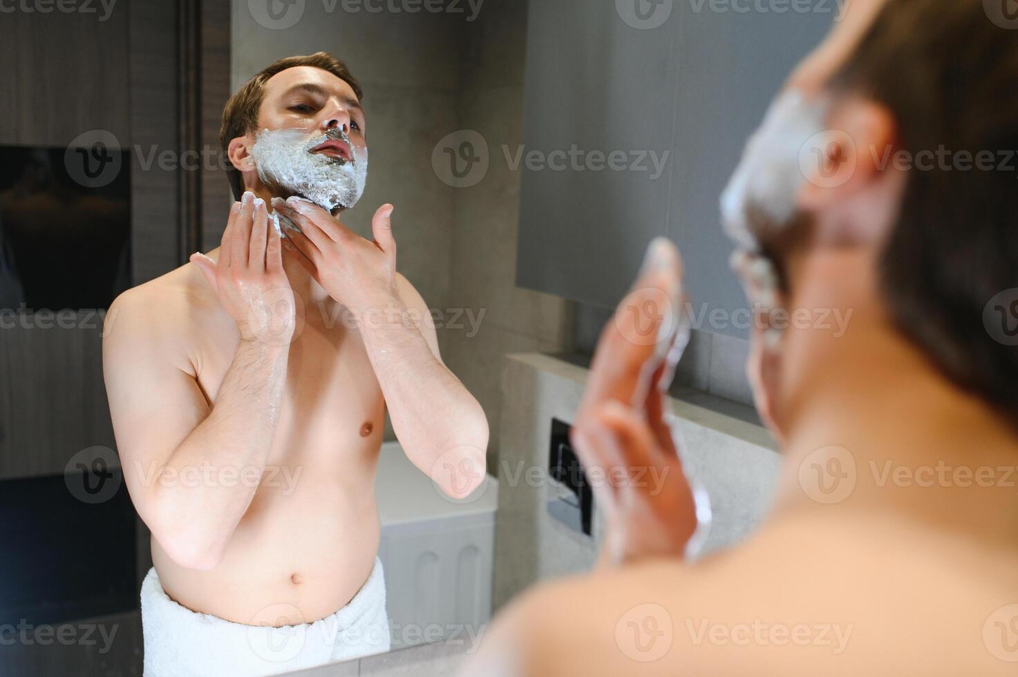 Shaving cream. Morning hygiene procedures. Grooming treatment. Handsome cheerful shirtless man showing applying foam on skin photo