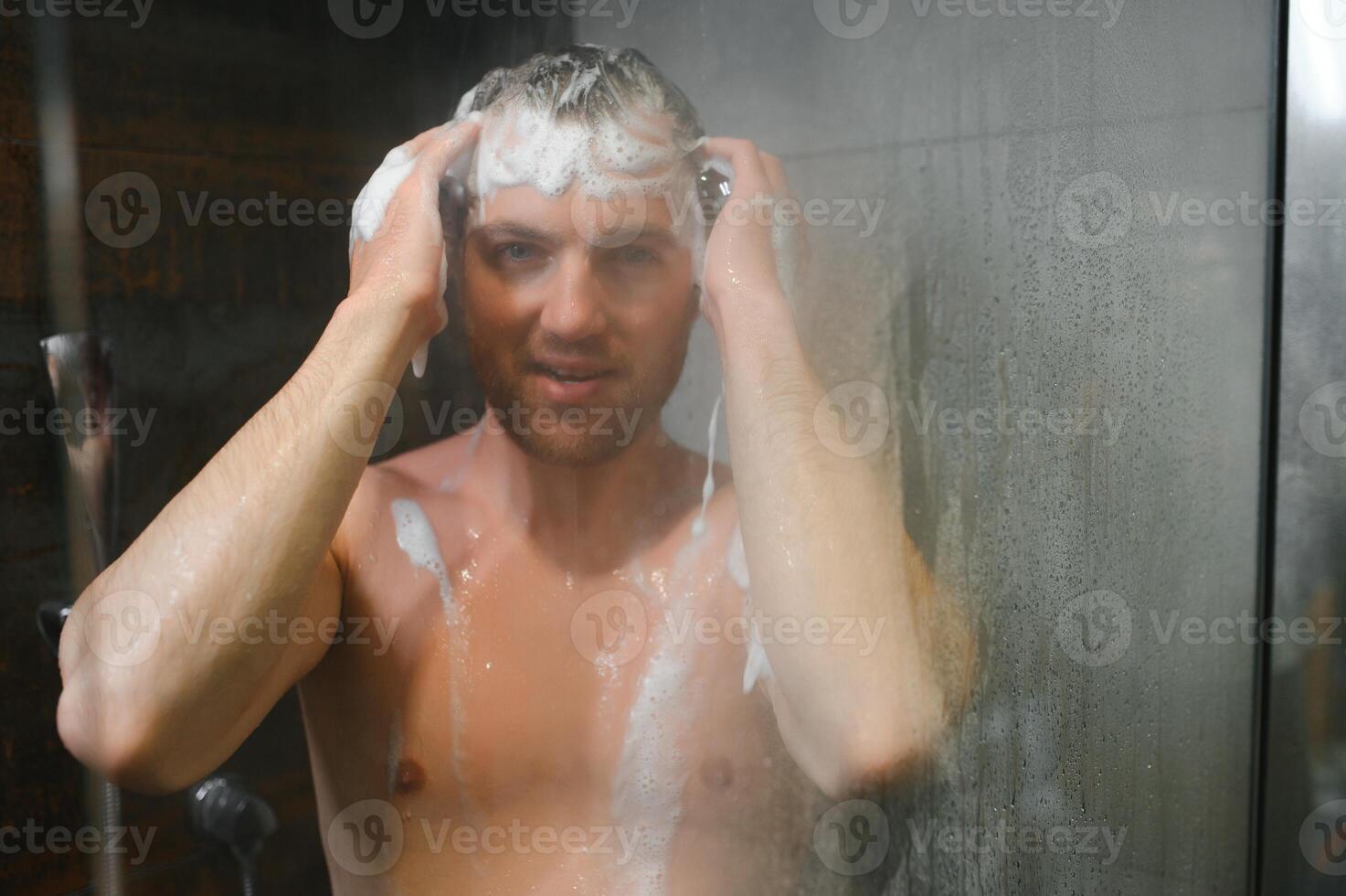 Relaxing after stressful day. Waist up portrait of naked muscular gentleman taking shower at home. photo