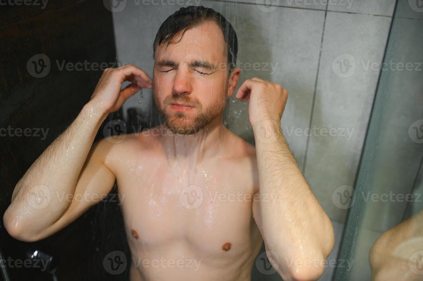 Relaxing after stressful day. Waist up portrait of naked muscular gentleman taking shower at home. photo