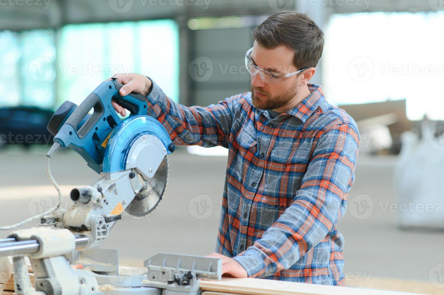 Wood cutting table with electric circular saw. Professional carpenter in uniform cutting wooden board at sawmill carpentry manufacturing . Sawing machine photo