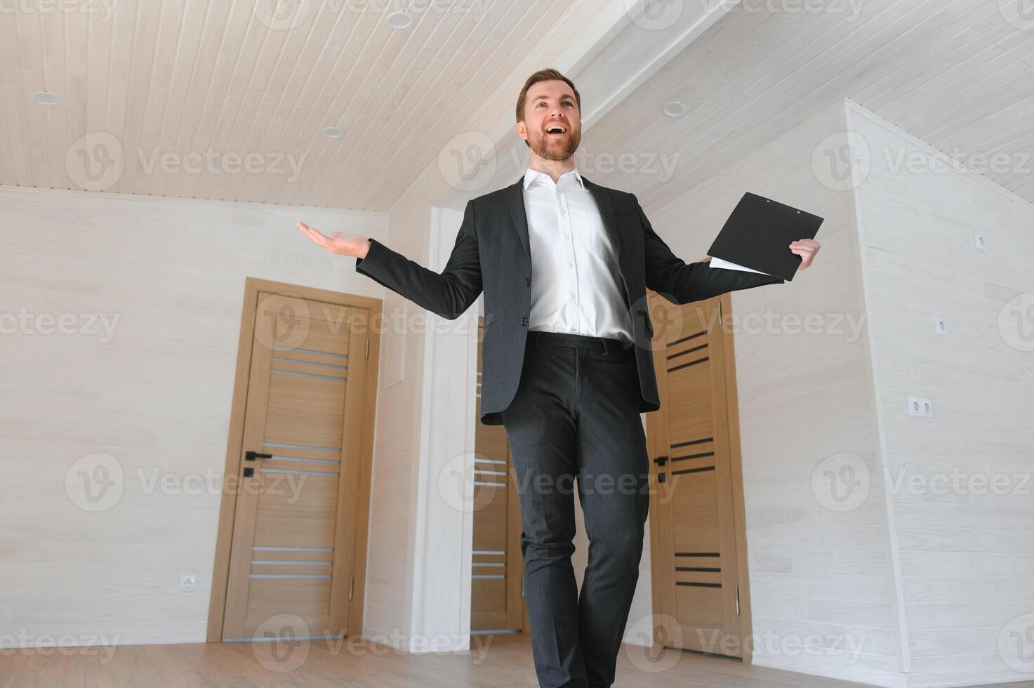 A successful real estate agent stands in a new modular building and offers a new home photo