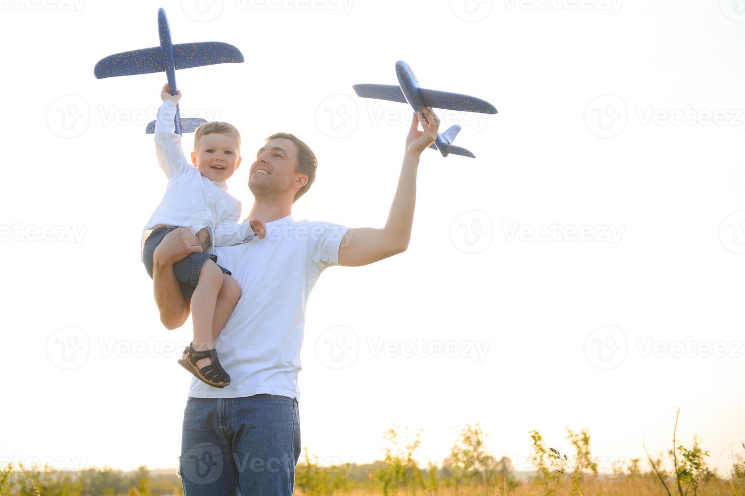 Happy father child moment. Father piggybacking his boy at sunset while he's playing with toy plane. photo